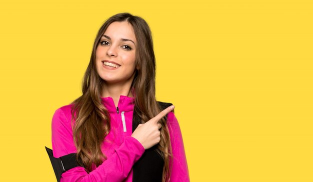 Jeune femme sportive pointant sur le côté pour présenter un produit sur un mur jaune isolé