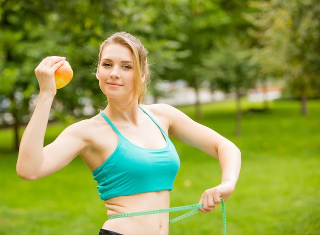 Jeune femme sportive avec pomme et ruban à mesurer dans le parc. Concept de mode de vie sain.