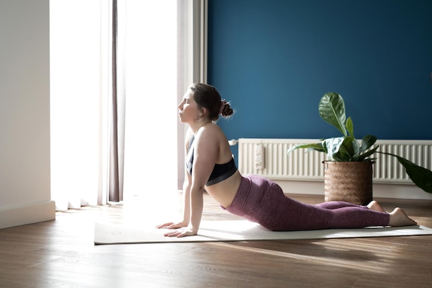 Jeune femme sportive pratiquant le yoga à la maison faisant de l'exercice pour chien orienté vers le haut urdhva mukha shvanasana