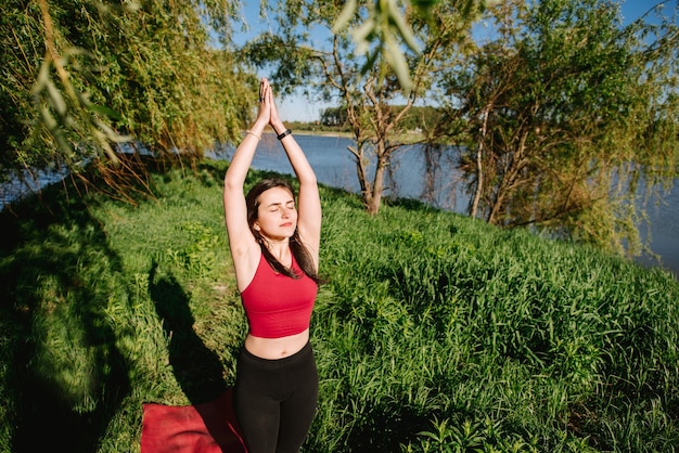 Jeune femme sportive pratiquant le yoga en plein air au bord du lac