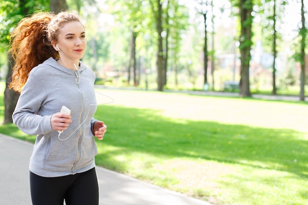 Jeune femme sportive qui court dans un parc verdoyant pendant l'entraînement du matin, espace pour copie