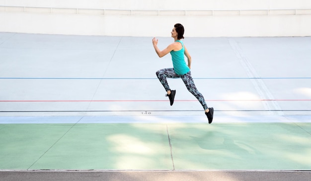 Jeune femme sportive qui court sur une piste toutes saisons au stade de la ville