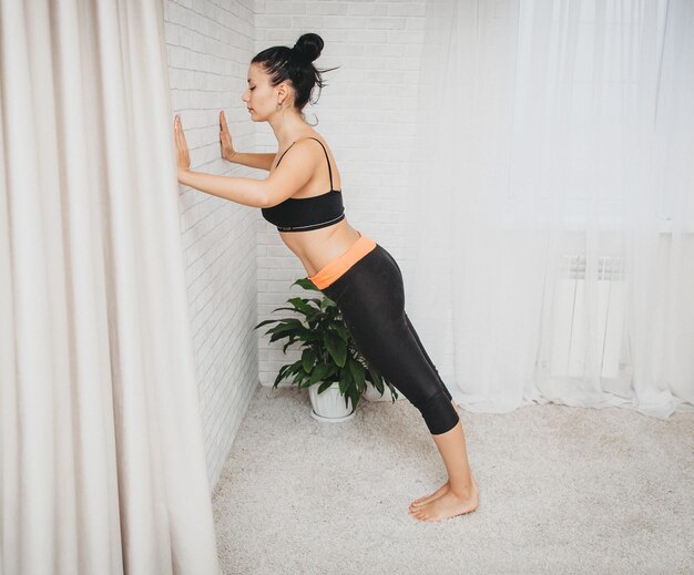 Une jeune femme sportive s'entraîne à la maison. fille mince, fait du sport sur un tapis de fitness à domicile, s'accroupit avec ses mains.