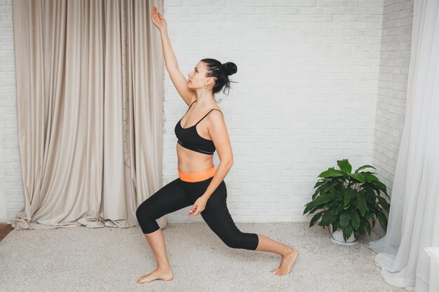 Une jeune femme sportive s'entraîne à la maison. fille mince, fait du sport sur un tapis de fitness à domicile, s'accroupit avec ses mains.