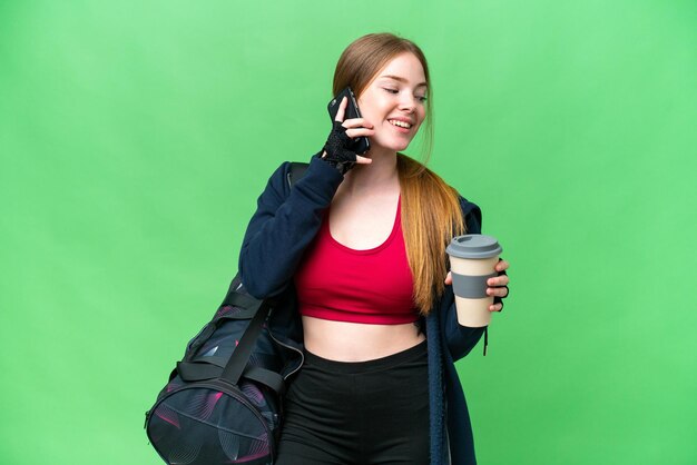 Jeune femme sportive avec sac de sport sur fond de clé chroma isolé tenant du café à emporter et un mobile