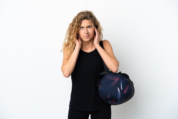 Jeune femme sportive avec sac de sport isolé sur fond blanc frustré et couvrant les oreilles