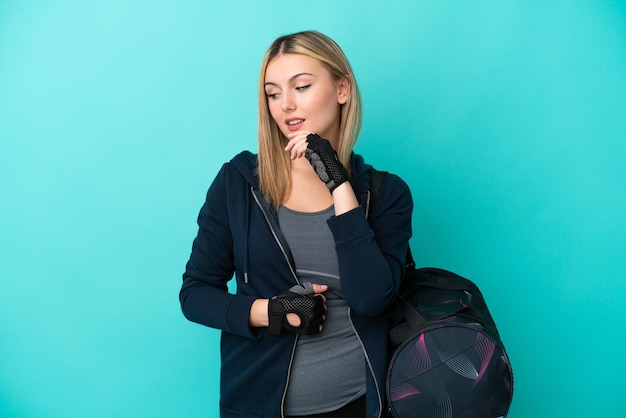 Jeune femme sportive avec sac de sport isolé sur fond bleu regardant sur le côté et souriant