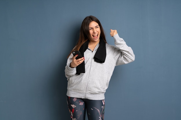 Jeune femme sportive avec téléphone en position de victoire