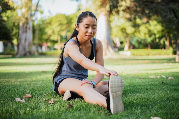 Jeune femme sportive touchant le bout de sa chaussure pour étirer sa jambe après avoir fait du jogging dans le parc