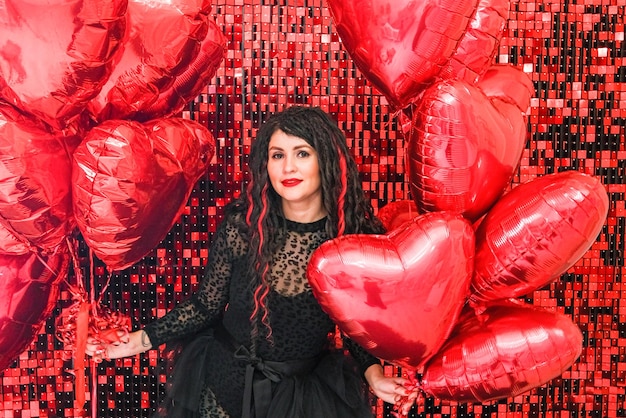 Jeune femme en stand noir avec des ballons en forme de coeur sur fond rouge