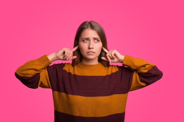 Une jeune femme stressée couvre les oreilles avec ses doigts.