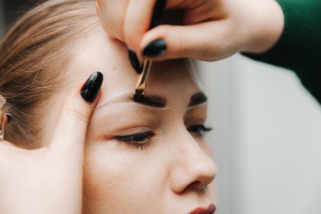 Une jeune femme subit une procédure de correction des sourcils dans un salon de beauté gros plan la fille peint ses sourcils dans le salon