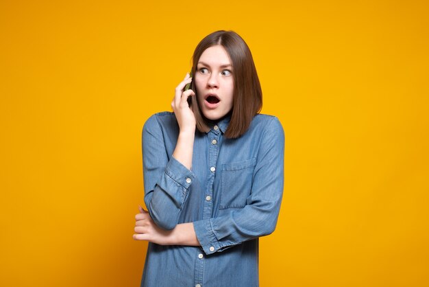 Jeune femme surprise occasionnelle lors d'un appel téléphonique, se dresse sur un jaune