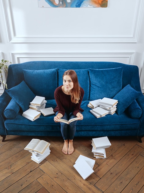 Jeune femme surprise parmi des piles de livres sur un canapé dans le salon