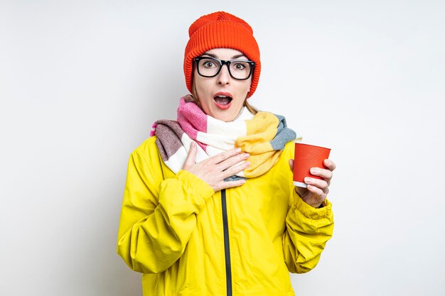 Jeune femme surprise avec une tasse de papier sur fond clair.