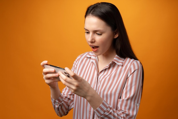 Jeune femme surprise utilisant un smartphone sur fond jaune