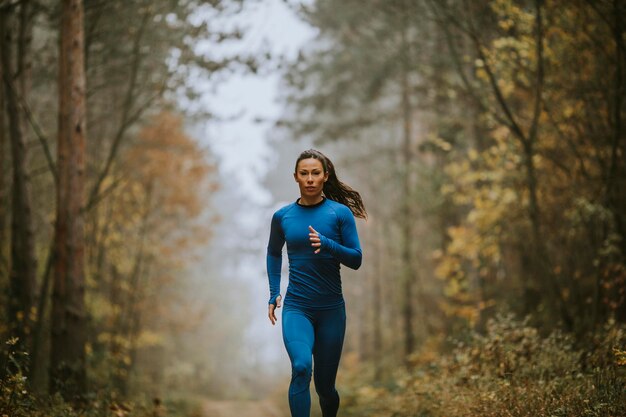 Jeune femme en survêtement bleu courant vers la caméra sur le sentier forestier à l'automne