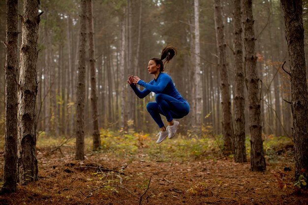 Jeune femme en survêtement bleu prenant le saut en hauteur sur le sentier forestier à l'automne