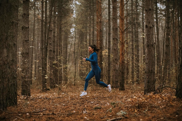 Jeune femme en survêtement bleu s'exécutant sur le sentier forestier à l'automne