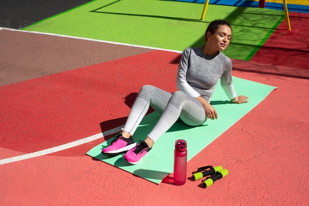 Jeune femme en survêtement gris est assis sur un tapis vert tenant avec la main