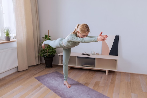 Une jeune femme en survêtement pratique le yoga à la maison