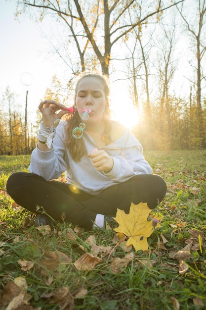 Jeune femme en sweat à capuche blanc soufflant des bulles de savon dans le parc d'automne