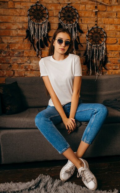 Jeune femme en t-shirt blanc posant en studio sur fond de mur de brique