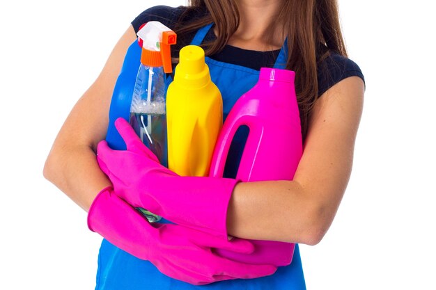 Jeune femme en T-shirt bleu et tablier avec des gants roses tenant des détergents sur fond blanc