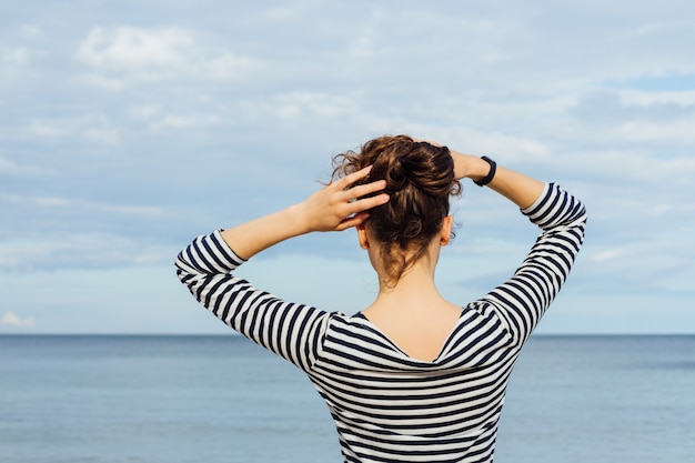 Jeune Femme En T-shirt Rayé Et Aux Cheveux Bouclés Regardant La Mer Et La Tenant Par La Tête