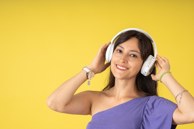 Jeune femme en t-shirt violet souriant tout en écoutant de la musique sur ses écouteurs blancs
