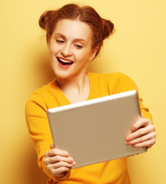 Jeune femme avec tablet pc sur fond jaune