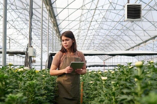 Une jeune femme avec une tablette debout entre deux parterres de fleurs longs et larges