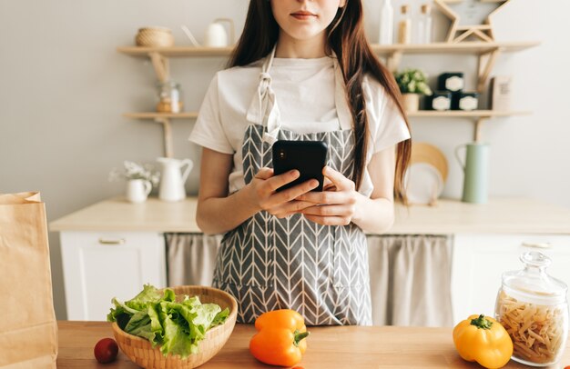 Jeune femme en tablier utilise le smartphone dans la cuisine