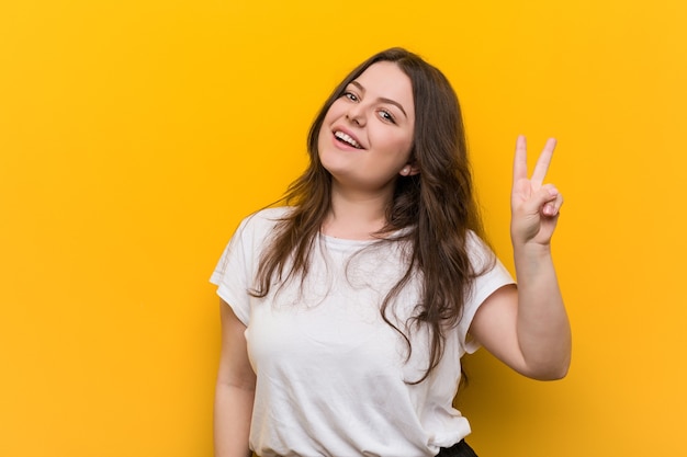 Jeune femme de taille plus courbée joyeuse et insouciante montrant un symbole de paix avec les doigts.