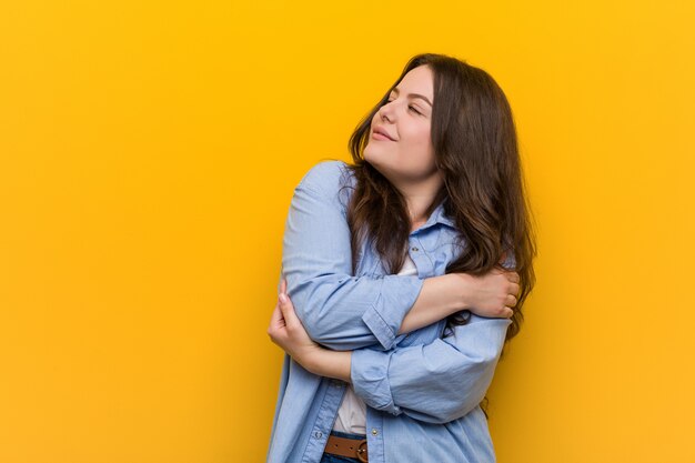 Jeune femme de taille plus galbée s'étreint, souriant insouciant et heureux.