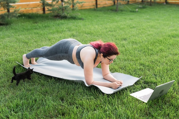 Jeune femme de taille plus en haut sportif et leggings debout en planche sur un tapis de yoga passant du temps sur