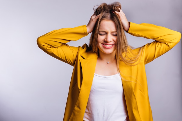 Jeune femme en tailleur pantalon jaune se tient la main dans ses cheveux et ferma les yeux. mal de crâne.