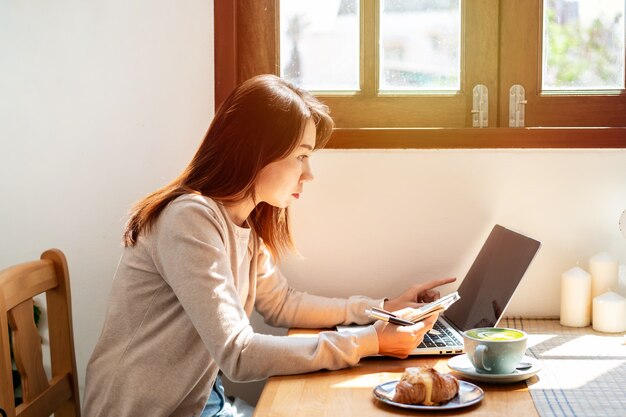 Jeune femme avec une tasse de café assise et travaillant sur un ordinateur portable au café