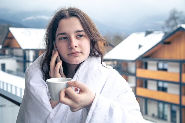 Une jeune femme avec une tasse de café sur le balcon en hiver dans les montagnes