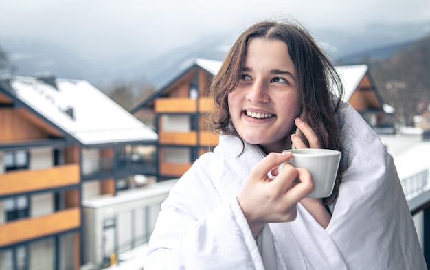 Une jeune femme avec une tasse de café sur le balcon en hiver dans les montagnes