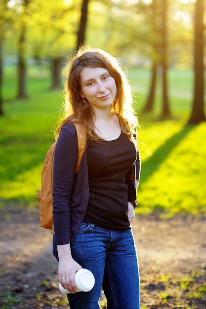 Jeune femme avec une tasse de café dans le parc du coucher du soleil