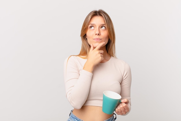 Jeune femme avec une tasse de café pensant, se sentant douteuse et confuse