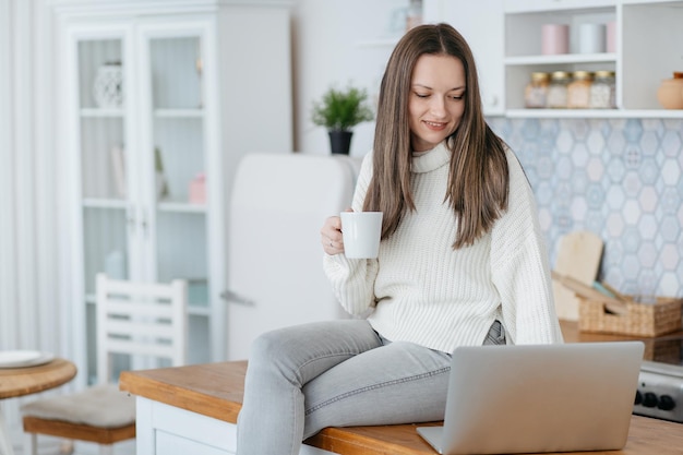 Jeune femme avec une tasse de café en regardant son écran d'ordinateur portable