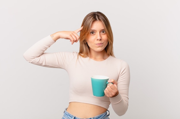 jeune femme avec une tasse de café se sentant confuse et perplexe, montrant que vous êtes fou