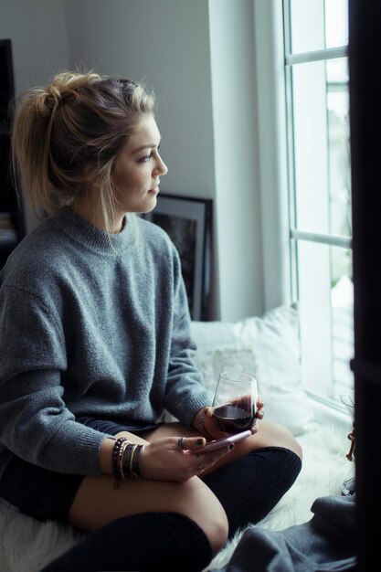 Jeune femme avec une tasse de café et smartphone regardant par la fenêtre