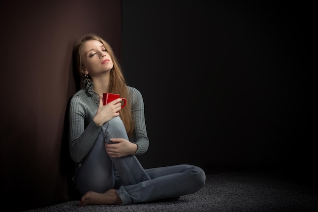 Jeune femme avec une tasse rouge assise sur le sol et rêvant