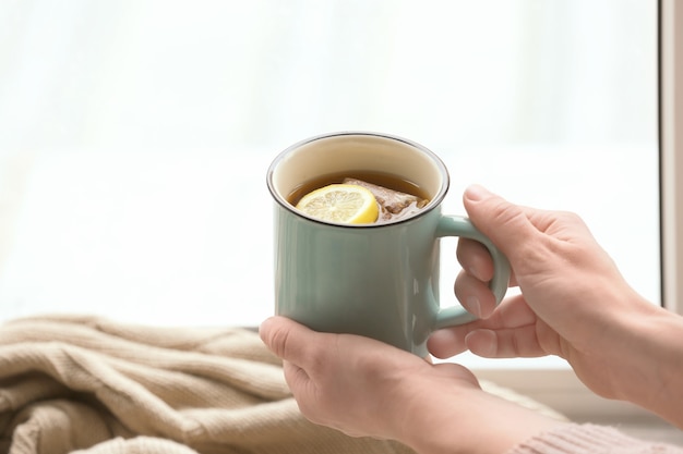 Jeune femme, à, tasse thé chaud, près, fenêtre, gros plan