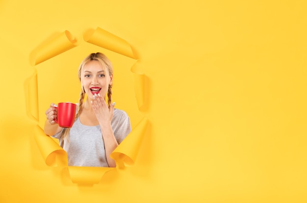 Jeune femme avec une tasse de thé sur une surface de papier jaune déchiré