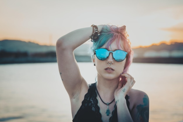 Jeune femme avec des tatouages et des cheveux roses et bleus jouant avec ses cheveux posant dans un parc d'attractions