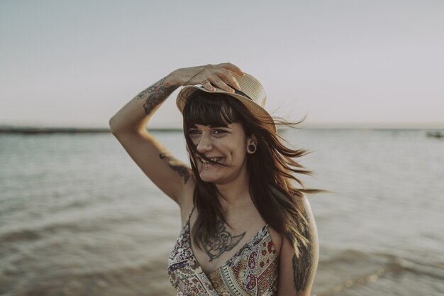 Jeune femme avec des tatouages portant une robe et un chapeau de paille sur l'océan flou